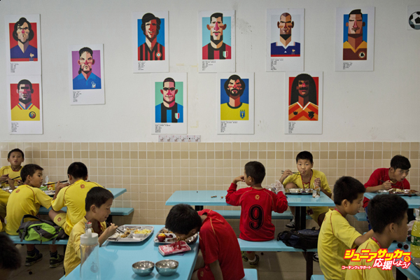 QINGYUAN, CHINA - JUNE 12:  Young Chinese football players eat lunch under caricatures of famous footballers in the canteen at the Evergrande International Football School on June 12, 2014 near Qingyuan in Guangdong Province, China. The sprawling 167-acre campus is the brainchild of property tycoon Xu Jiayin, whose ambition is to train a generation of young athletes to establish China as a football powerhouse. The school is considered the largest football academy in the world with 2400 students, more than 50 pitches and a squad of Spanish coaches through a partnership with Real Madrid. (Photo by Kevin Frayer/Getty Images)