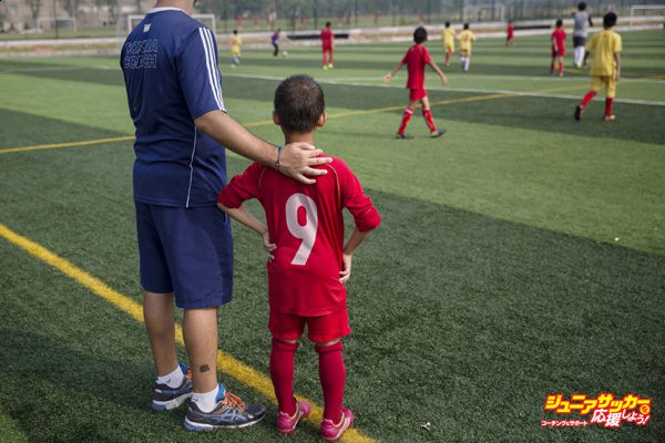 QINGYUAN, CHINA - JUNE 14:  A coach from Real Madrid stands with a young Chinese student before subbing him to a training match at the Evergrande International Football School on June 14, 2014 near Qingyuan in Guangdong Province, China. The sprawling 167-acre campus is the brainchild of property tycoon Xu Jiayin, whose ambition is to train a generation of young athletes to establish China as a football powerhouse. The school is considered the largest football academy in the world with 2400 students, more than 50 pitches and a squad of Spanish coaches through a partnership with Real Madrid. (Photo by Kevin Frayer/Getty Images)